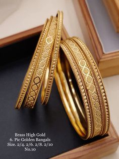 two gold colored bangles sitting on top of a black surface next to a wooden box