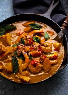 a bowl filled with curry and meat on top of a blue table cloth next to a wooden spoon