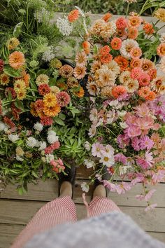 a person standing next to a bunch of flowers on top of a wooden floor with their feet propped up