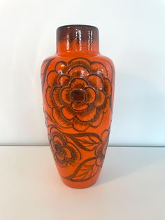 an orange vase sitting on top of a white table next to a black and red flower