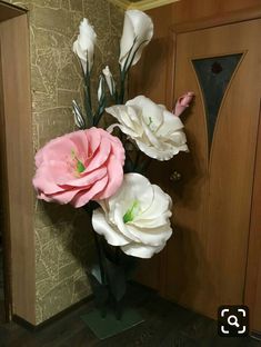 three pink and white flowers are in a vase on the floor next to a door