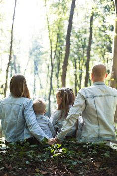 the family is sitting on the ground in the woods looking at the trees and leaves