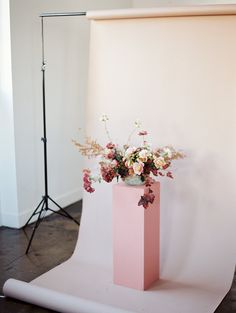 a pink vase filled with flowers on top of a wooden floor next to a white wall