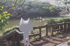 a cat statue sitting on the side of a wooden fence next to a body of water