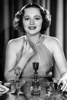 an old photo of a woman sitting at a table in front of some wine glasses