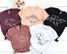 four t - shirts with dinosaur designs on them sitting next to a white furnishing