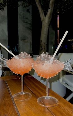 two glasses filled with drinks sitting on top of a wooden table next to each other