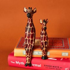 two giraffe figurines sitting on top of some books and orange background