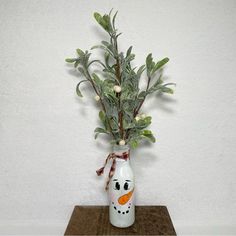 a white vase with some plants in it on a wooden table next to a wall