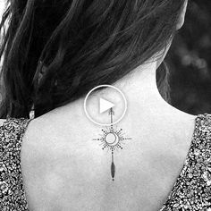 the back of a woman's neck with an arrow and sun tattoo on it