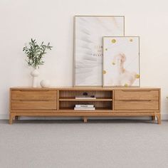 a wooden entertainment center with two pictures on the wall and a potted plant next to it