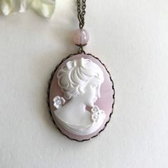 "Here is lovely cameo necklace in a shade of soft pink. This cameo depicts a beautiful woman adorned with white flowers, and has very nice detailing throughout. This large cameo is set in an oxidized solid brass setting and is suspended from a pretty pink glass bead and comes on a long brass chain. Cameo is made from resin. As with all of my jewelry this necklace will be shipped in a lovely gift box. This pretty necklace makes a wonderful gift! Cameo Pendant measures: 1 1/4\" across x 1 5/8\" lo Vintage Pink Oval Necklace, Antique Pink Cameo Jewelry, Pink Cameo Necklace For Gifts, Antique Pink Necklaces For Wedding, Antique Handmade Pink Necklaces, Antique Handmade Pink Necklace, Pink Antique Handmade Necklace, Handmade Pink Antique Necklace, Pretty Necklace