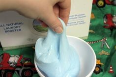 a hand is dipping blue liquid into a white bowl on top of a green tablecloth