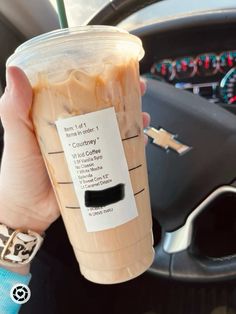 a person holding up a cup of coffee in their hand while sitting in a car