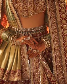 a woman in a red and gold bridal outfit with her hands on her hip