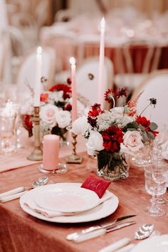 the table is set with white and red flowers in vases, silverware, and candles