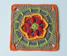 a crocheted square with an orange, yellow and blue design on the center