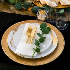 a place setting with gold rimmed plates and greenery