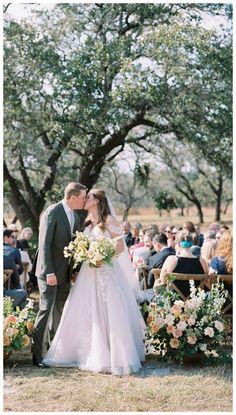 a bride and groom kissing in front of an outdoor wedding ceremony with flowers on the aisle