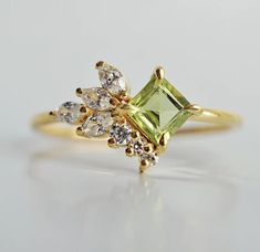 a yellow gold ring with green and white stones on it's side, sitting on a table