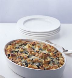 a casserole dish with bread and spinach in it on a white table