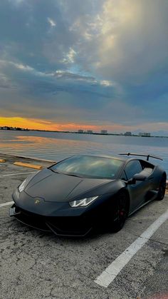 a black sports car is parked in the parking lot by the water at sunset or dawn