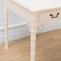 a white table with two drawers sitting on top of a hard wood floor next to a wall