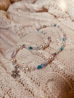 a white knitted blanket with a beaded necklace on it and a cross charm