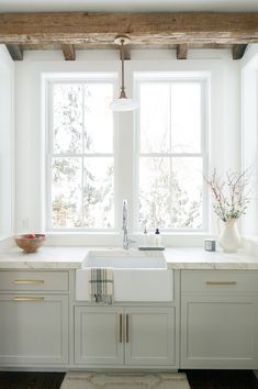 a kitchen with white cabinets and wooden beams in the window sill, along with a rug on the floor