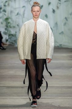 a model walks down the runway wearing an oversize sweater and sheer - pleaed skirt