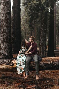 a man and woman sitting on a log in the middle of a forest with trees