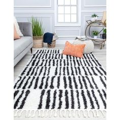 a black and white rug with an orange pillow on the floor next to a couch