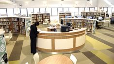 a woman standing in front of a library with lots of bookshelves and desks