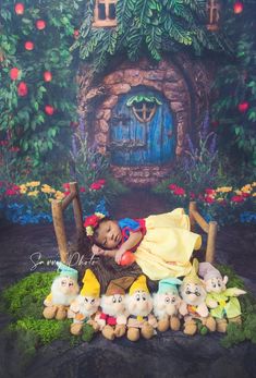 a child laying on top of stuffed animals in front of a fake house with trees and flowers