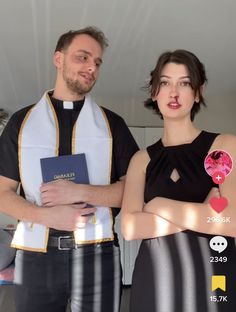 two people standing next to each other in front of a white wall and one is holding a book