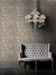 a couch sitting in front of a chandelier next to a wall with an ornate design on it