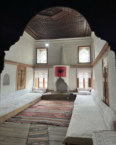 the inside of a room with several beds and rugs on the floor in front of two windows