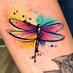 a colorful dragonfly tattoo on the right thigh with watercolor splashes around it