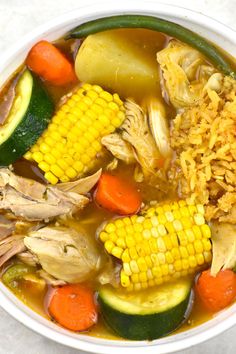 a bowl filled with soup and vegetables on top of a white countertop next to a spoon