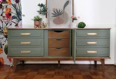 a green dresser with gold handles and drawers in front of a floral wallpapered background