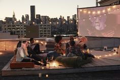 group of people sitting on top of a roof watching a movie in the city at night