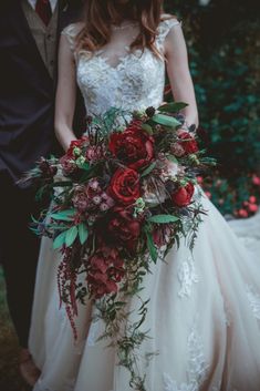 a bride and groom standing next to each other in front of some bushes with red flowers