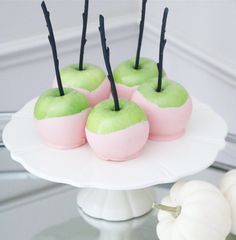 four green apples with black sticks sticking out of them on a white cake platter