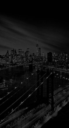 black and white photograph of the brooklyn bridge at night with city lights in the background