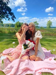 two women sitting on a blanket in the grass, one is covering her face with her hand