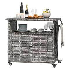 a wicker bar cart with wine glasses and plates on the top, next to bottles