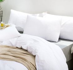 a bed with white sheets and pillows on top of it next to a plant in a vase