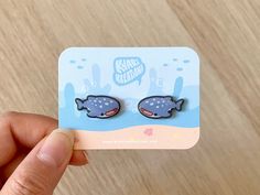 a person holding up a pair of fish shaped studs on top of a card