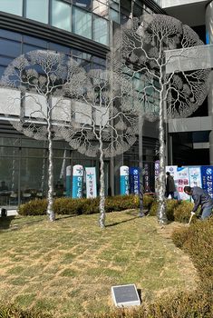 a man is working on some metal trees in front of a building with glass windows