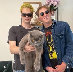 two men standing next to each other holding a cat